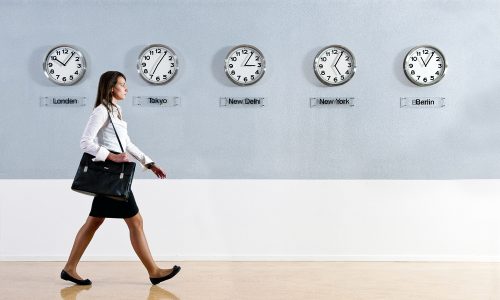 Business woman walking hurrily past a row of clocks showing the time in various parts of the world. Business, travel, time concept